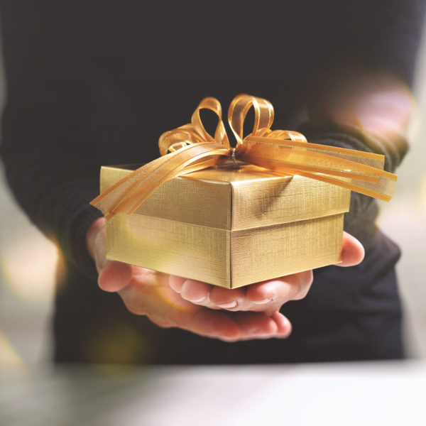 gift giving,man hand holding a gold gift box in a gesture of giving.blurred background,bokeh effect